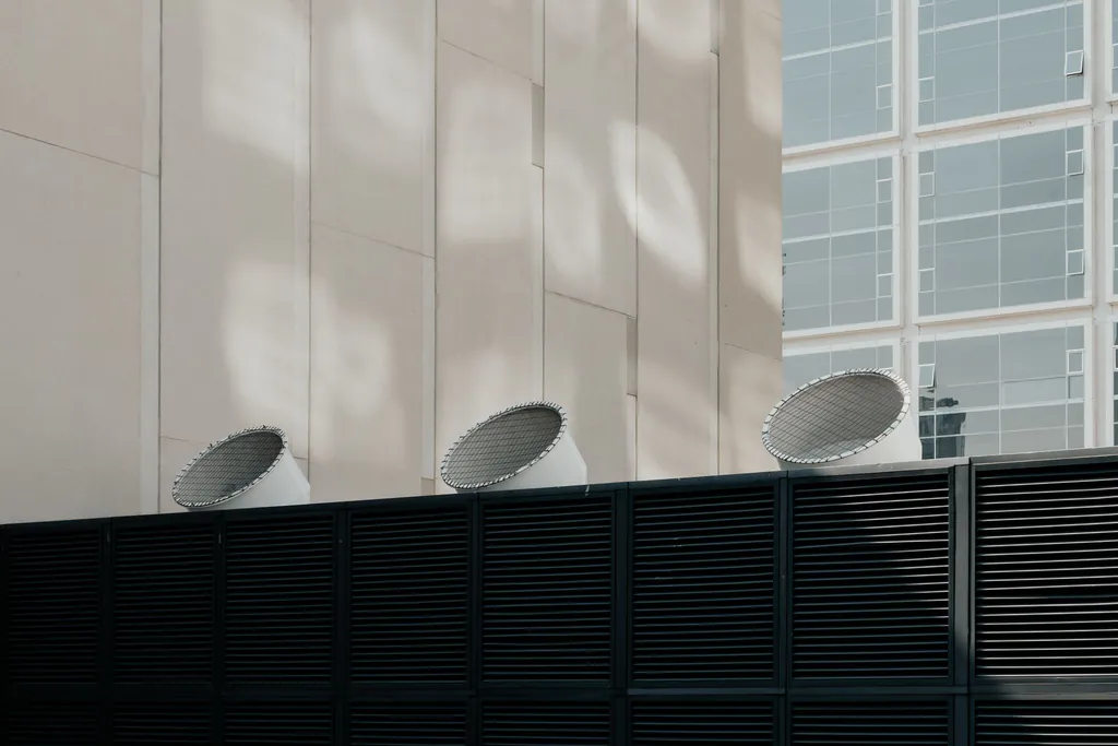 Three round ventilation hoods on a building roof, behind a dark louvered screen